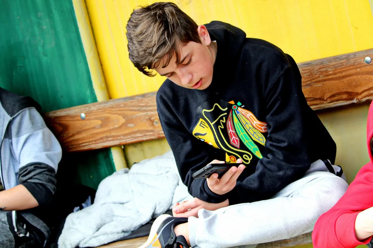 A boy sitting on a bench looking at a smartphone