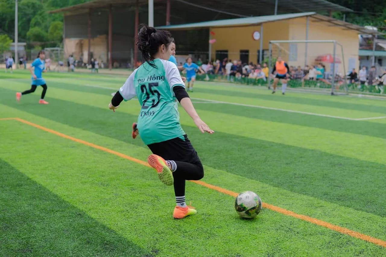 A young female football player dribbling the ball on a pitch
