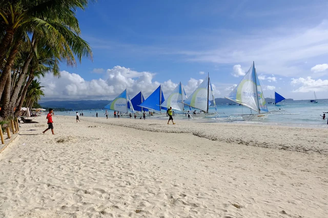 Sailboats lined up along White Beach in Boracay under a blue sky