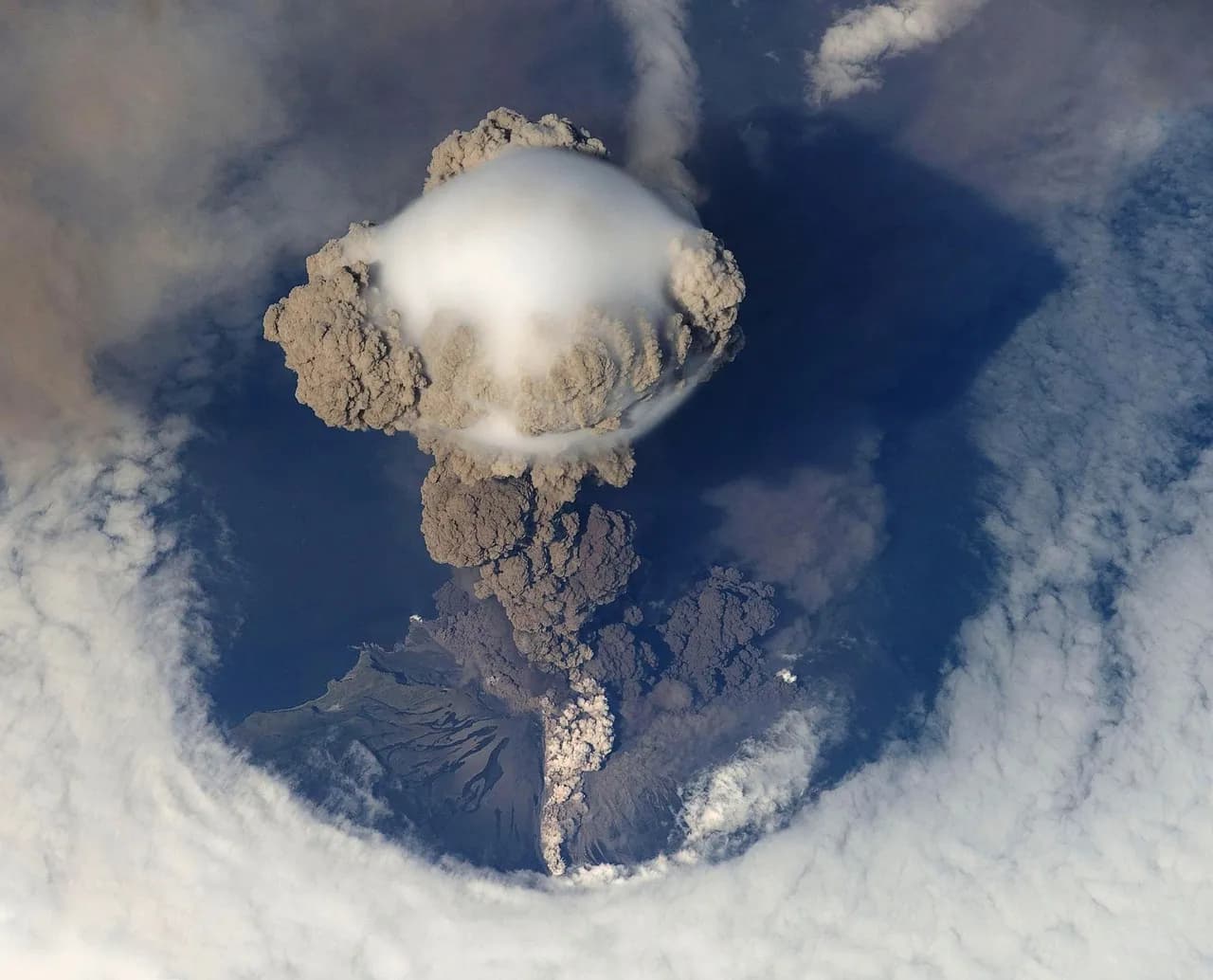 Aerial view of a volcanic ash plume rising through clouds
